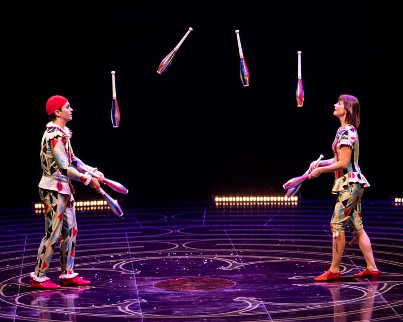 Two performers juggling multiple clubs.